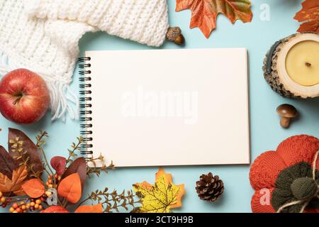 Thanksgiving day background. Falling leaves, notepad, knitted scarf and wooden candle on blue background. Stock Photo