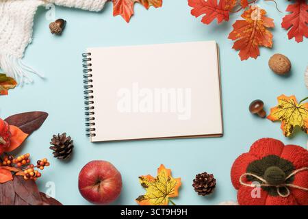 Thanksgiving day background. Falling leaves, notepad, knitted scarf and wooden candle on blue background. Stock Photo