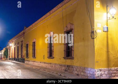 A yellow building with a dark street in front of it. The street is lit up by street lights. Historic center of Queretaro, colonial architecture, decor Stock Photo