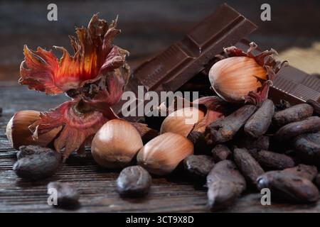 Broken dark chocolate with cocoa beans and hazelnuts on a wooden table Stock Photo