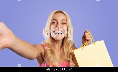 Excited woman holding colorful shopping bags taking selfie Stock Photo