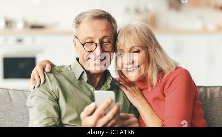 Happy Senior Couple Using Smartphone Together Sitting At Home Stock Photo
