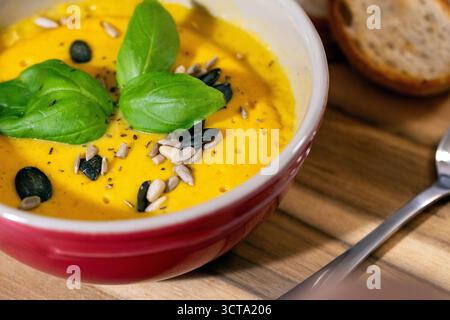 Delicious pumpkin soup served in red bowls, garnished with fresh basil leaves, sunflower and pumpkin seeds Stock Photo