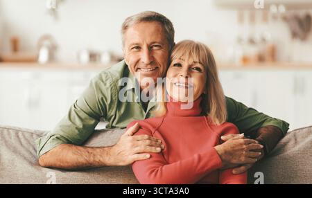 Happy Senior Couple Embracing Sitting On Sofa At Home Stock Photo