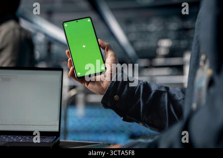 Close up of server farm software developer using mockup phone, waiting for code to finish compile. Data center employee checking mobile apps on green screen smartphone to relax Stock Photo