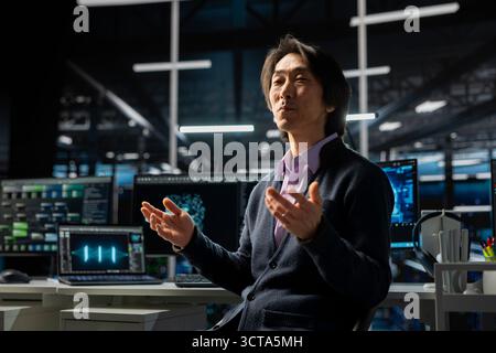 Computer scientist in server room using device to review infrastructure diagnostics. Asian senior programmer in high tech data center analyzing performance data to maintain system uptime Stock Photo
