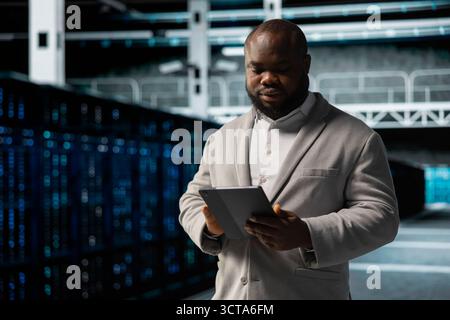Data center employee fixing network issues affecting rigs performance, scripting automated workflows. Technician running system diagnostic tests, evaluating reports on tablet Stock Photo