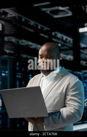 Server hub developer using laptop to fix network issues affecting storage arrays, doing backups. Programmer in data center runs system diagnostic tests, scanning hardware logs for faults Stock Photo