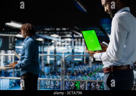 African american technician using copy space display on tablet, solving software development tasks on industrial platform. Young man visualizing infrastructure engineering in server room. Stock Photo