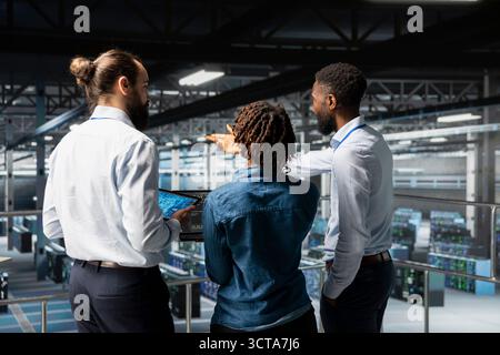 Data center staff on industrial platform collaborating to maintain servers using artificial intelligence. Engineers doing teamwork to support infrastructure AI deep learning automatization. Stock Photo