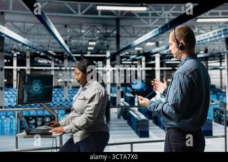 Server hub engineers providing remote tech support using headset and artificial intelligent tools. Teamworking employees coordinating IT maintenance tasks using AI technology Stock Photo