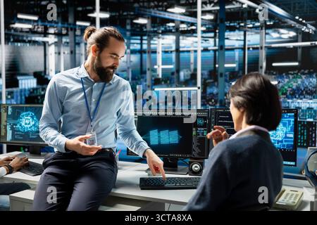 Teamworking data center colleagues managing AI training datasets using PC. Team of engineers doing brainstorming, overseeing machine learning in server room supporting scalable equipment for AI apps Stock Photo