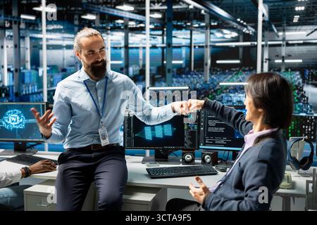 Coworkers coding in data center doing fist bump, pleased after updating AI automation scripts. Happy server room colleagues celebrating programming artificial intelligence algorithms Stock Photo