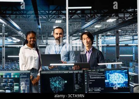 Portrait of smiling multiethnic engineers in data center troubleshooting server connectivity issues using AI. Upbeat multiracial technicians in diverse server room auditing systems for vulnerabilities Stock Photo