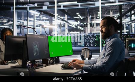Engineer using green screen mockup PC in data center to update servers tech, configuring equipment using software tools. Server room worker reviewing hardware analytics on chroma key PC, camera A Stock Photo