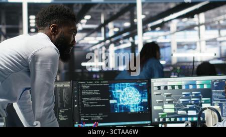 Technician in wheelchair and data center manager using AI node tree software to minimize system downtime. Server hub employee in disability and team leader using visual programming tool, camera B Stock Photo