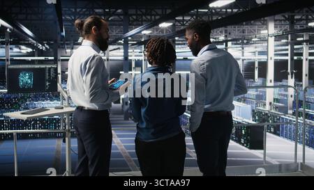 Software developers in data center monitoring AI LLM visualization. Server farm teamworking colleagues doing brainstorming, overseeing rigs powering machine learning processes, Stock Photo