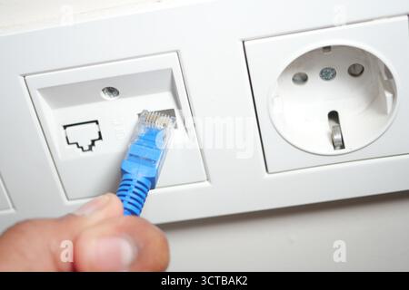 Connecting a blue Ethernet cable to a wall port in a home Stock Photo
