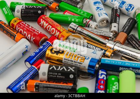 A collection of different batteries is haphazardly arranged on a white surface, showcasing various brands and types including alkaline and lithium opt Stock Photo