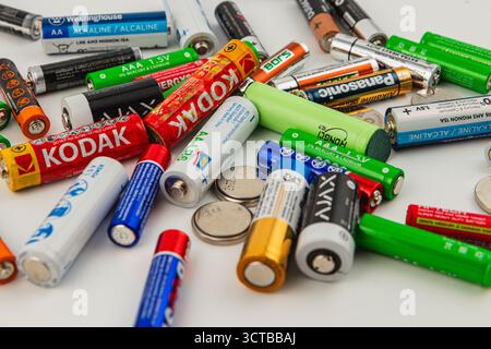 A collection of batteries in different sizes and colors is spread out on a flat surface alongside several coins. The batteries include AA, AAA, and 9V Stock Photo