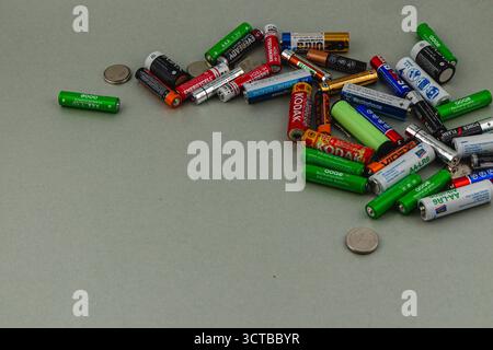 A collection of various batteries spreads out on a light gray surface, alongside several coins. The arrangement features different brands and sizes, s Stock Photo
