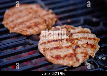Two meat patties cooking on hot barbecue grill with visible grill marks. Concept of food, barbecue and outdoor cooking. Stock Photo