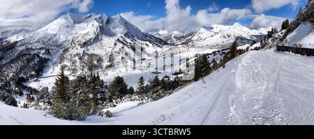 Skier standing on a snowy mountain slope with picturesque snow - capped peaks in the background under a blue sky with clouds. Austria - Obertauern Stock Photo