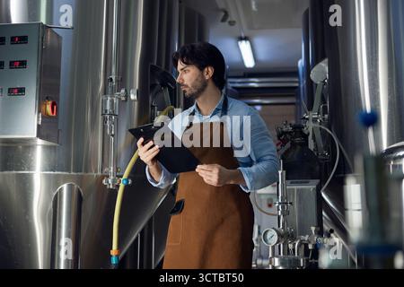 A man wearing an apron is utilizing a clipboard in a factory setting Stock Photo
