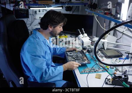 A skilled technician diligently repairing laptop while working under a microscope Stock Photo