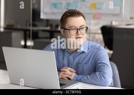 Thoughtful young professional man with Down syndrome working at laptop Stock Photo