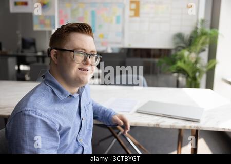 Positive professional man with Down syndrome sitting at work table Stock Photo