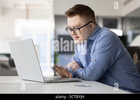 Positive inclusive company worker with Down syndrome typing on laptop Stock Photo