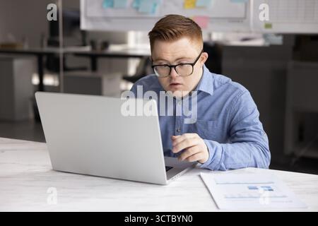 Focused inclusive company employee with Down syndrome typing on laptop Stock Photo