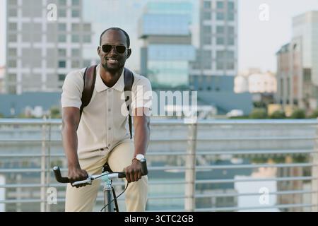 Young Adult Black Man Riding Bicycle Outdoors near Modern Urban Buildings Stock Photo