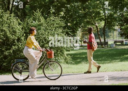Young Caucasian Woman Riding Bicycle Past Middle Aged Black Man Walking Outdoors Stock Photo