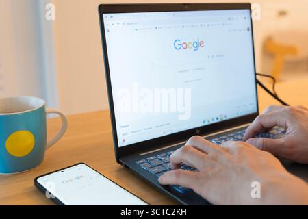 October 5, 2025 Bangkok, Thailand : Close-up of a person's hands typing on a laptop keyboard, performing a search on the Google homepage. A smartphone Stock Photo