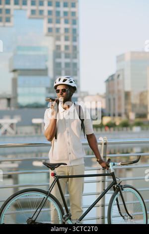 Young Adult Black Man Standing Outdoors Using Smartphone near Bicycle Stock Photo
