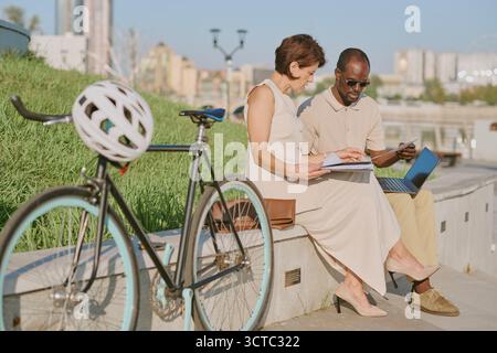 Middle Aged Caucasian Woman and Black Man Collaborating Outdoors with Laptop Stock Photo