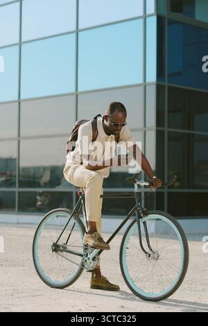 Young Adult Black Man Using Smartphone While Sitting on Bicycle Outdoors Stock Photo