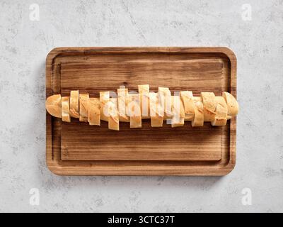 Baguette bread sliced into pieces resting on a rectangular wooden cutting board. Preparing fresh appetizers or a meal Stock Photo