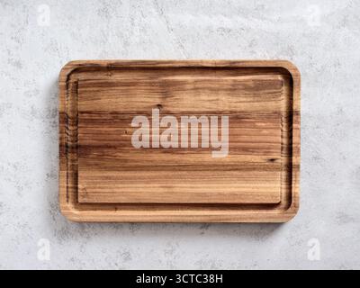 Empty wooden cutting board on a gray textured surface, providing a rustic and natural surface for food preparation or presentation Stock Photo