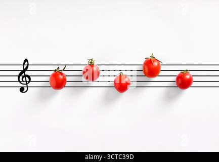 Cherry tomatoes forming musical notes on a white background staff with a G clef, representing a creative food concept Stock Photo