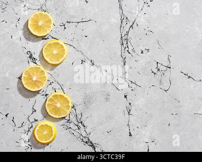 Vertical line of fresh yellow lemon slices on a grey marble background with black veins, offering a vibrant contrast Stock Photo