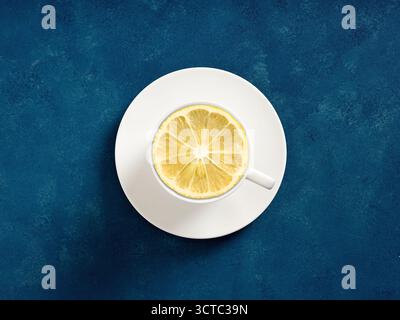 Lemon slice resting in a white ceramic teacup with saucer, centered on a textured deep blue surface, viewed from above Stock Photo