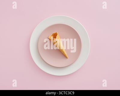 Empty waffle cone resting on a pink plate, set on a larger white plate with a pastel pink background. Minimal dessert concept Stock Photo