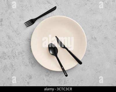 Empty plate featuring minimalist black plastic fork, knife, and spoon on a concrete table, symbolizing temporary dining or zero waste Stock Photo