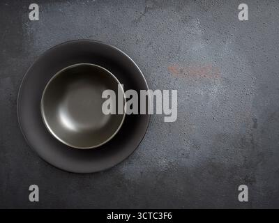 Empty dark plate and bowl creating a minimalist food photography setup on a rustic, textured background with copy space Stock Photo