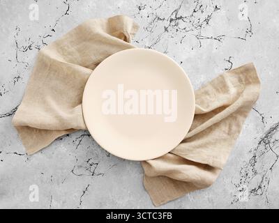Empty beige plate on a natural linen napkin, resting on a gray marble background. Top view presenting copy space. Food mockup table setting. Stock Photo