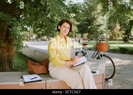 Portrait of Middle Aged Caucasian Woman Writing in Notebook Outdoors Stock Photo