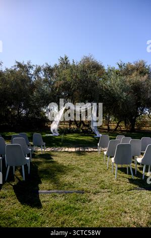 Outdoor wedding ceremony with white chairs on green lawn in front of fabric arch. A location for an outdoor marriage registration ceremony in a garden Stock Photo
